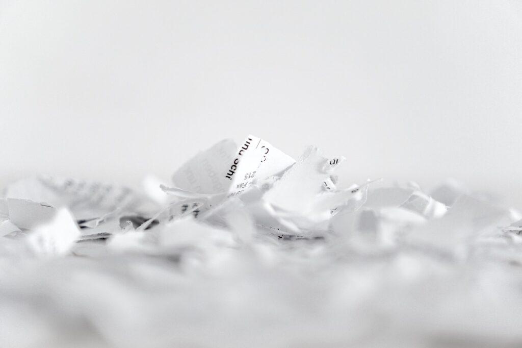 Photograph of a pile of shredded white paper on a white surface, with a plain white background.