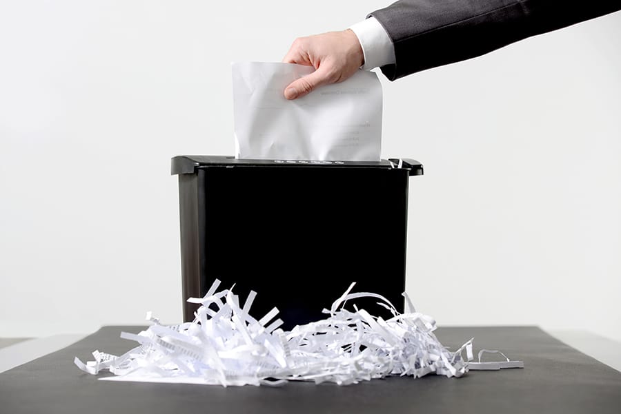 Hand of businessman putting a document in paper shredder with pile of previously shredded paper